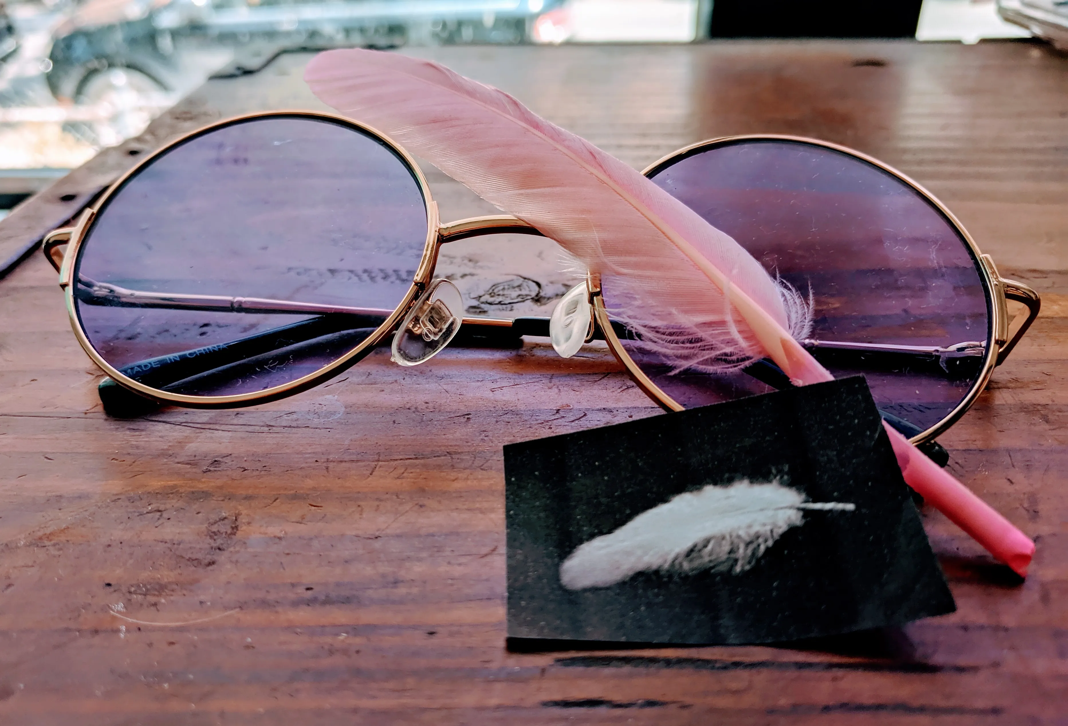Close up of purple glasses, a pink feather, and a picture of a feather